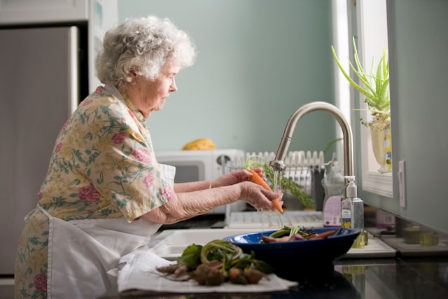 Elderly woman preparing vegetables in her home kitchen, living independently and aging in place